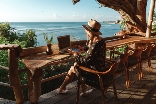 Frau sitzt mit ihrem Laptop in traumhafter Kulisse mit Blick auf das Meer